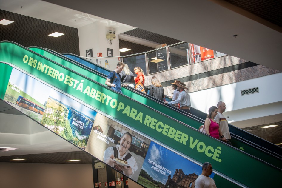 Imagem de uma escada rolante adesivada com elementos da campanha do turismo do governo do Estado.