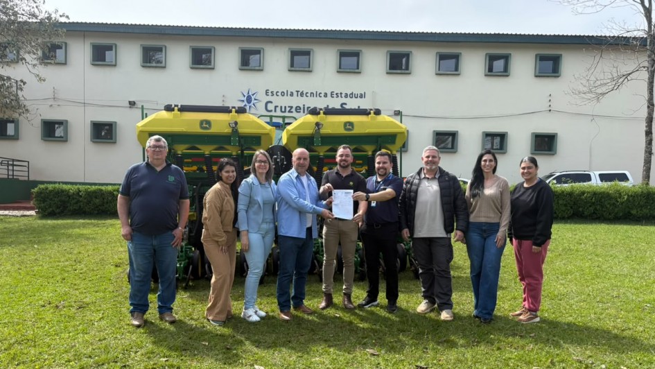 Foto mostra autoridades reunidas e segurando o documento em frente &agrave; escola. Eles est&atilde;o em um gramado verde. A escola tem fachada branca. 