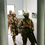 Foto mostra policiais penais com fardas, capacete e m&aacute;scara, usando armas longas, est&atilde;o no corredor de uma unidade prisional.