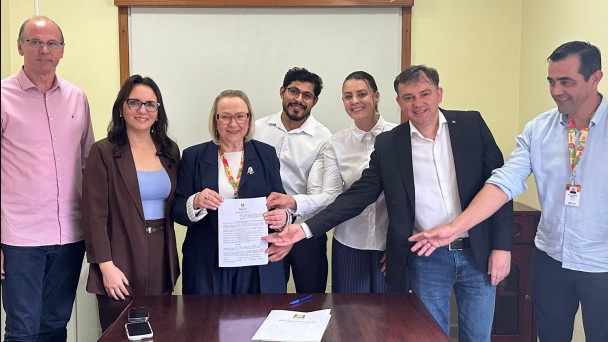Foto mostra secret&aacute;ria e representantes do hospital exibindo o documento assinado.